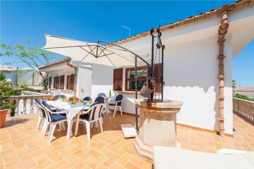 A sunny outdoor dining terrace with a table beneath a large shade umbrella.