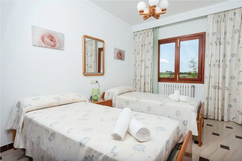 A bright bedroom with two beds, floral curtains, and a wooden-framed window.