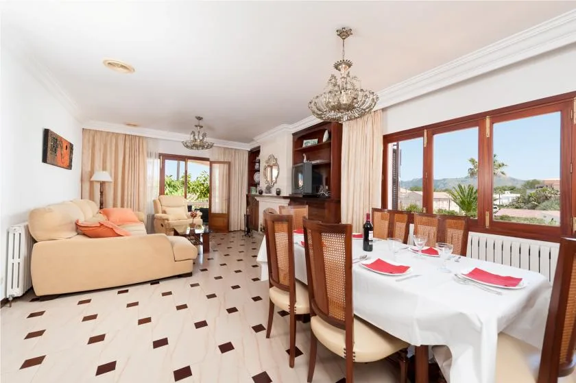 Un luminoso salón-comedor con la mesa puesta junto a grandes ventanales.