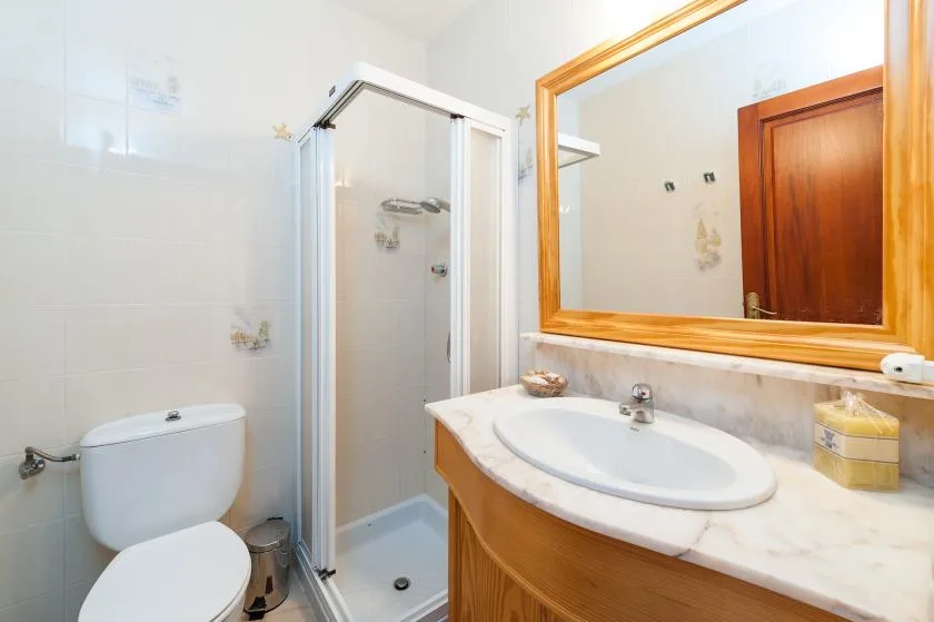 A bathroom with a glass shower, toilet, and sink beneath a large mirror.