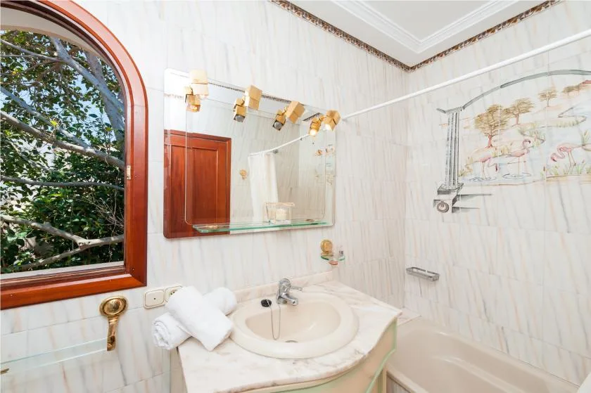 A bright bathroom with a sink beneath a mirror and a bathtub beside it.