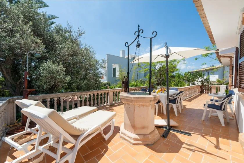 A sunny outdoor terrace with lounge seating, a tiled floor, and potted plants.