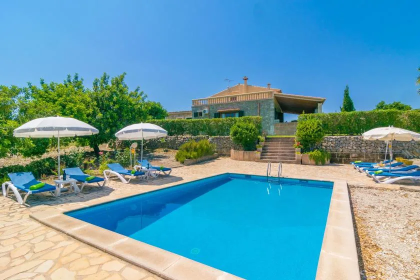 Una piscina ocupa una terraza soleada junto a una casa y tumbonas.
