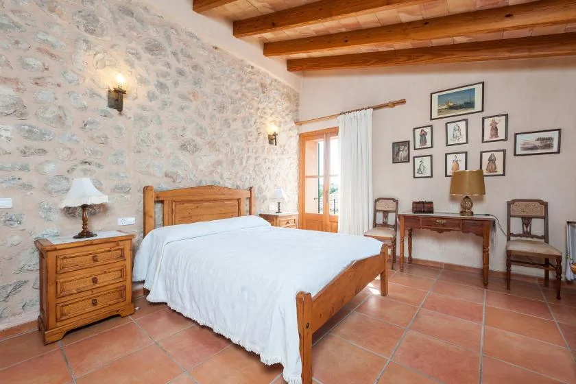 Dormitorio con cama de madera, suelo de baldosas de terracota y vigas vistas en el techo.
