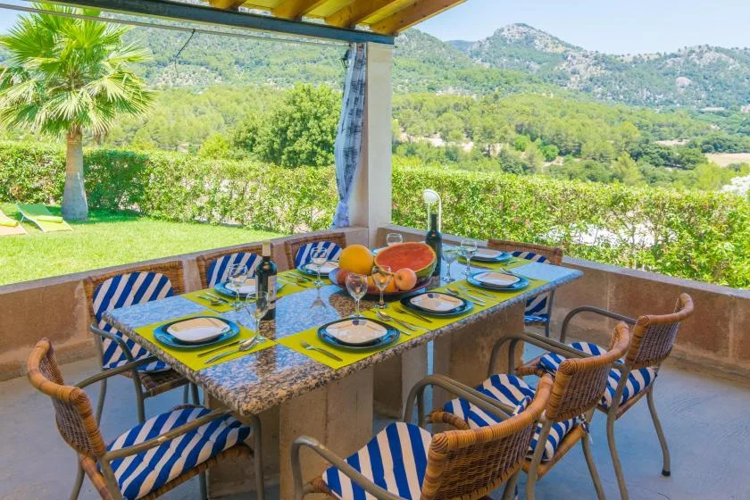Comedor exterior cubierto con la mesa puesta y vistas a colinas verdes.