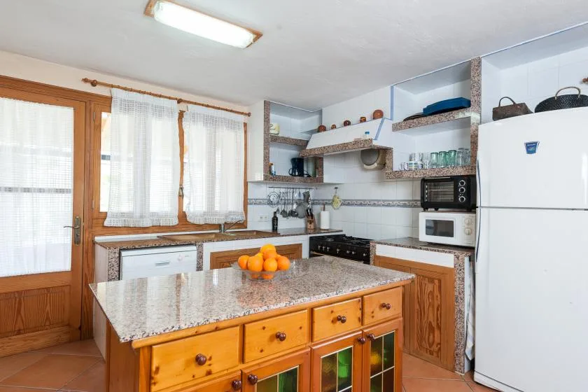 Una cocina luminosa con gabinetes de madera, una isla central y grandes ventanas con cortinas.