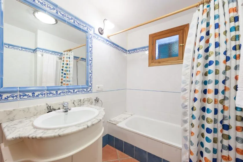 Un baño alicatado con lavabo, bañera y cortina de ducha estampada.