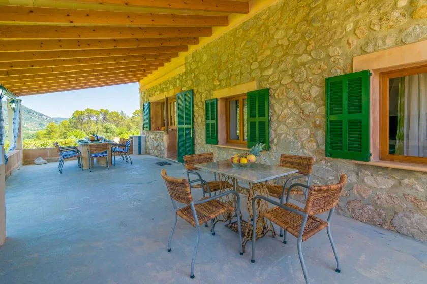 Una terraza cubierta de piedra con asientos al aire libre y contraventanas verdes.