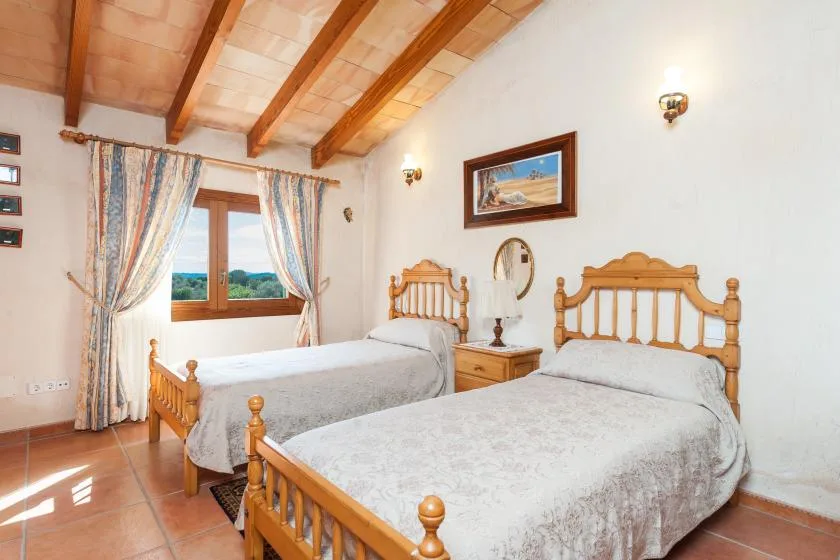Dormitorio con dos camas, cabeceros de madera y una ventana con cortinas.
