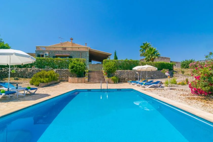 Una piscina al aire libre junto a un patio ajardinado con tumbonas y sombrillas.
