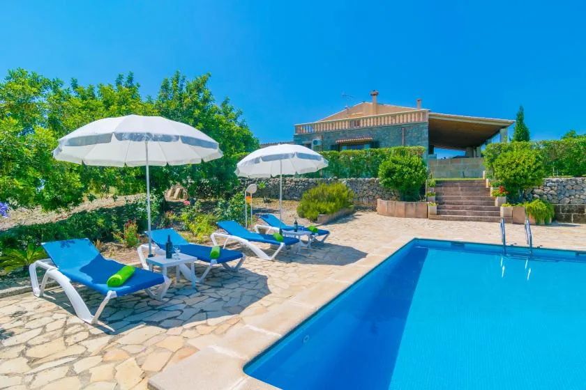Piscina al aire libre junto a un patio pavimentado con tumbonas y sombrillas.