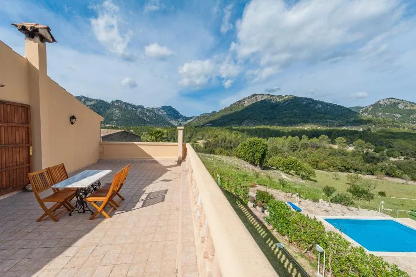 Una terraza embaldosada con asientos al aire libre da a un valle verde y una piscina.