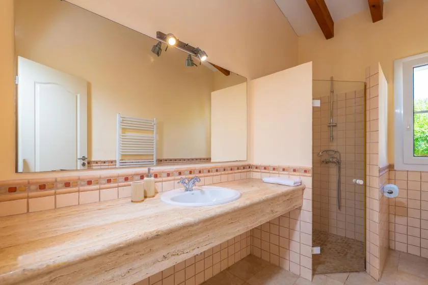 Un baño alicatado con una encimera larga, lavabo y zona de ducha abierta.
