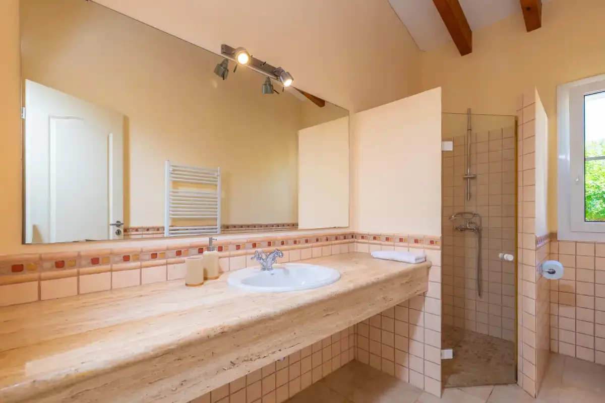Un baño alicatado con un lavabo largo, un lavamanos y una ducha de vidrio.