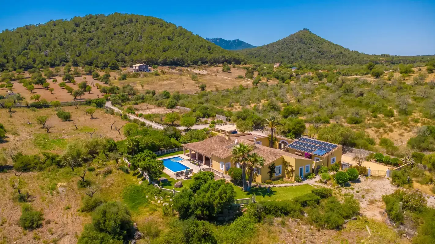 Una casa con piscina se encuentra entre campos secos y colinas verdes.