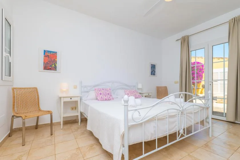 Un dormitorio luminoso con una cama blanca, mesitas de noche y puertas corredizas de vidrio.