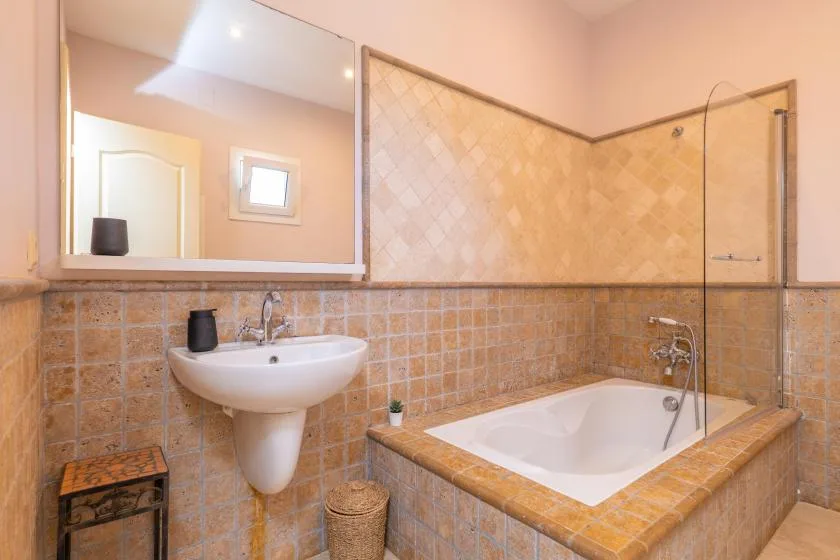 Un baño revestido de azulejos con lavabo suspendido y bañera.
