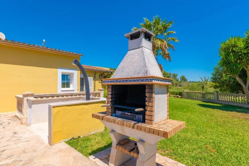Una parrilla exterior está junto a una casa amarilla y un patio con césped.