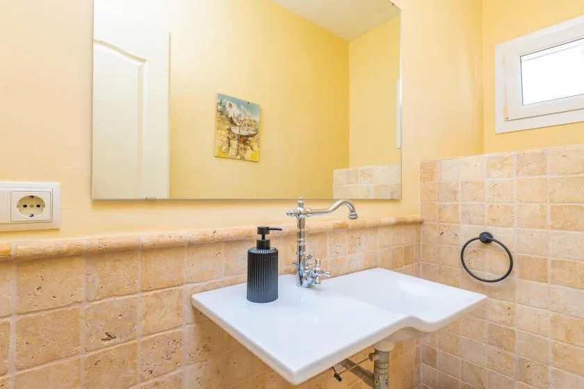 Un lavabo de baño con un espejo amplio y una ventana pequeña.
