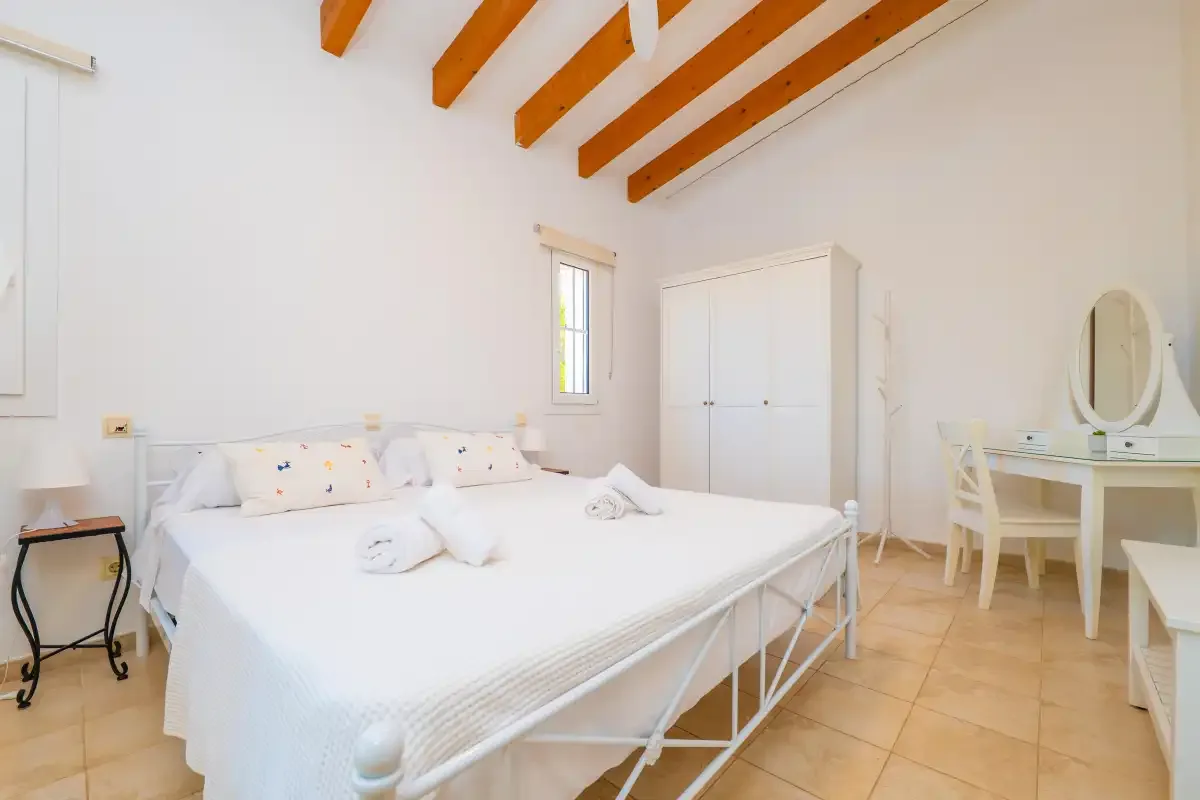 Un dormitorio luminoso con una cama grande, un armario blanco y vigas expuestas en el techo.