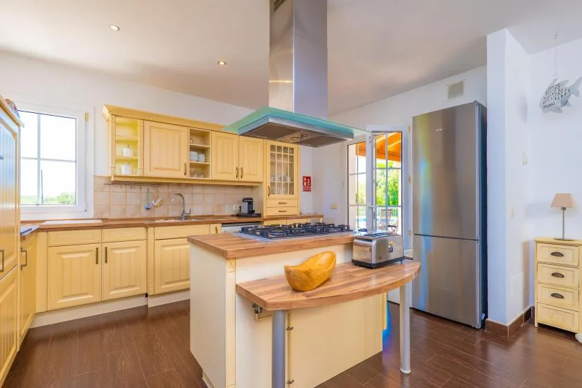 Una cocina luminosa con gabinetes de madera clara, una isla central y electrodomésticos de acero inoxidable.