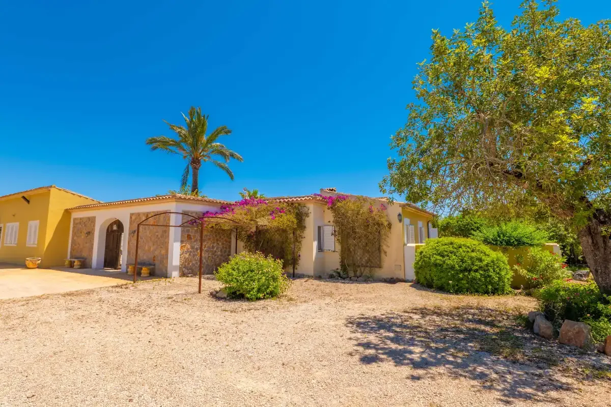 Una casa baja está junto a un amplio patio de grava con arbustos y árboles.