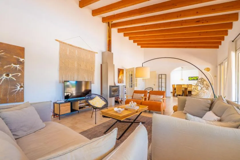 Una sala de estar luminosa con sofás, un televisor y vigas de madera vistas en el techo.