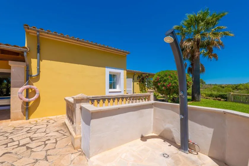 Una zona de ducha exterior soleada junto a un edificio amarillo, con una palmera cerca.