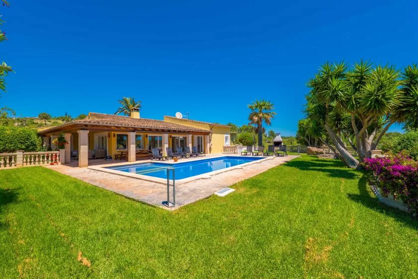 Una casa y una piscina se encuentran junto a un amplio césped bajo un cielo despejado.