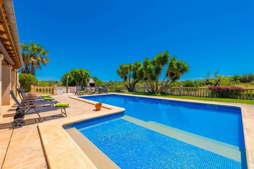 Una piscina al aire libre junto a un patio pavimentado con asientos y jardines.
