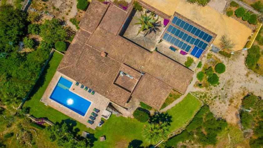 Vista aérea de una casa, una piscina y paneles solares entre jardines.