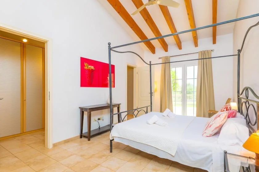 Un dormitorio luminoso con una cama blanca y ventanas altas.