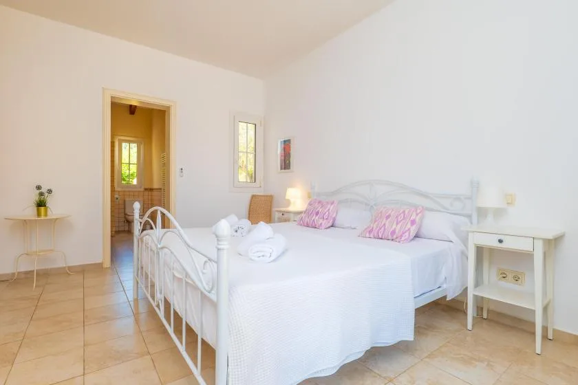 Un dormitorio luminoso con una cama blanca y una puerta abierta.