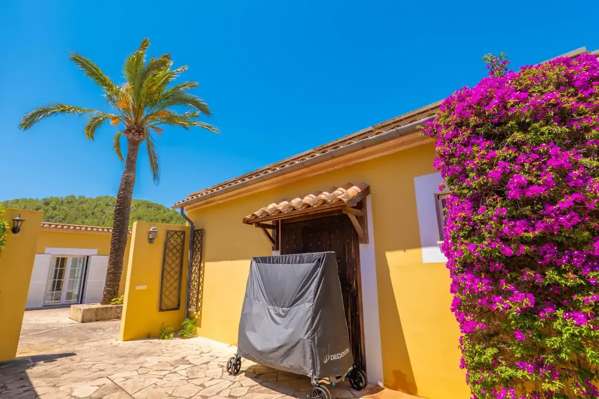 Entrada de una casa amarilla con una parrilla cubierta al aire libre y buganvilla en flor.