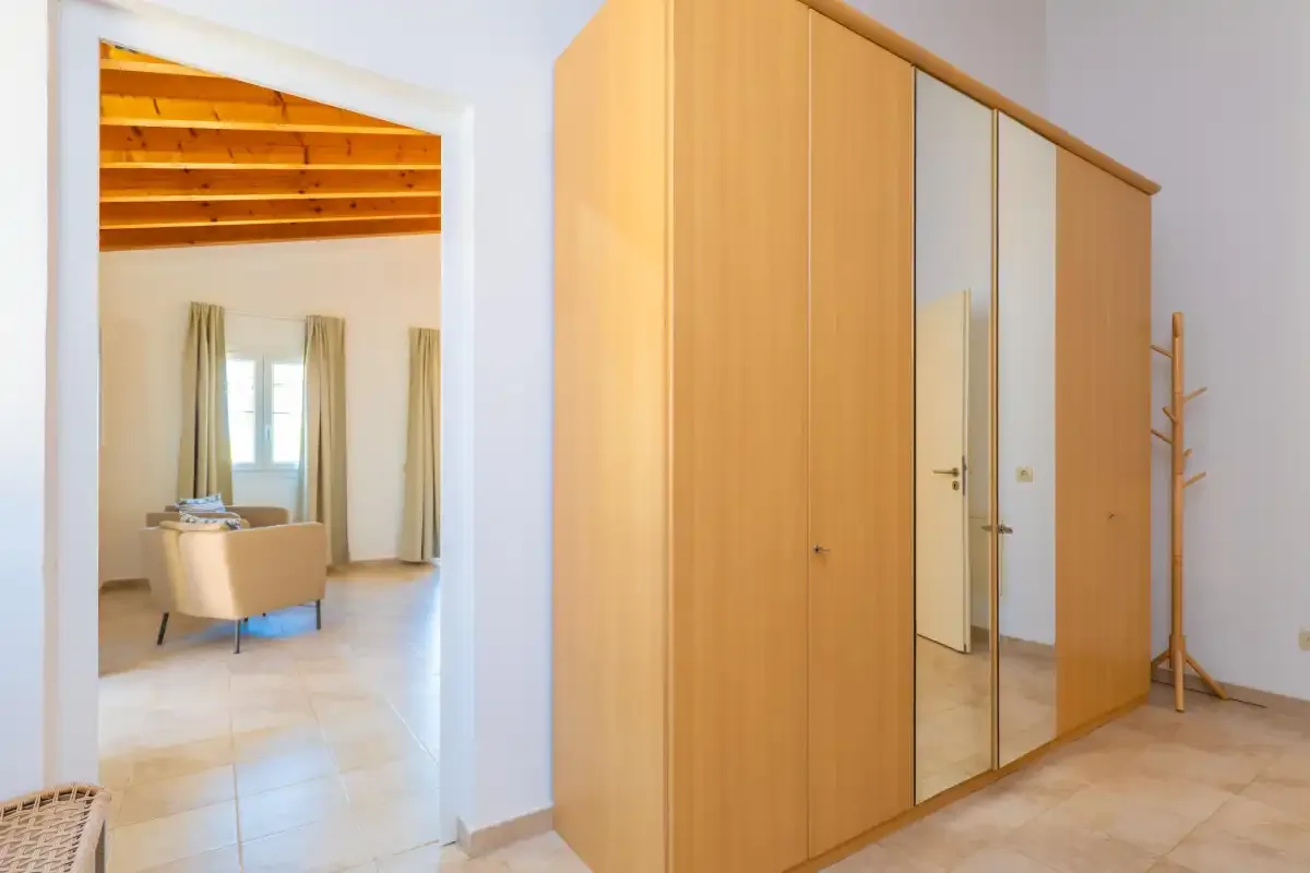 Un armario de madera con puertas de espejo está junto a una puerta abierta a una zona de estar.