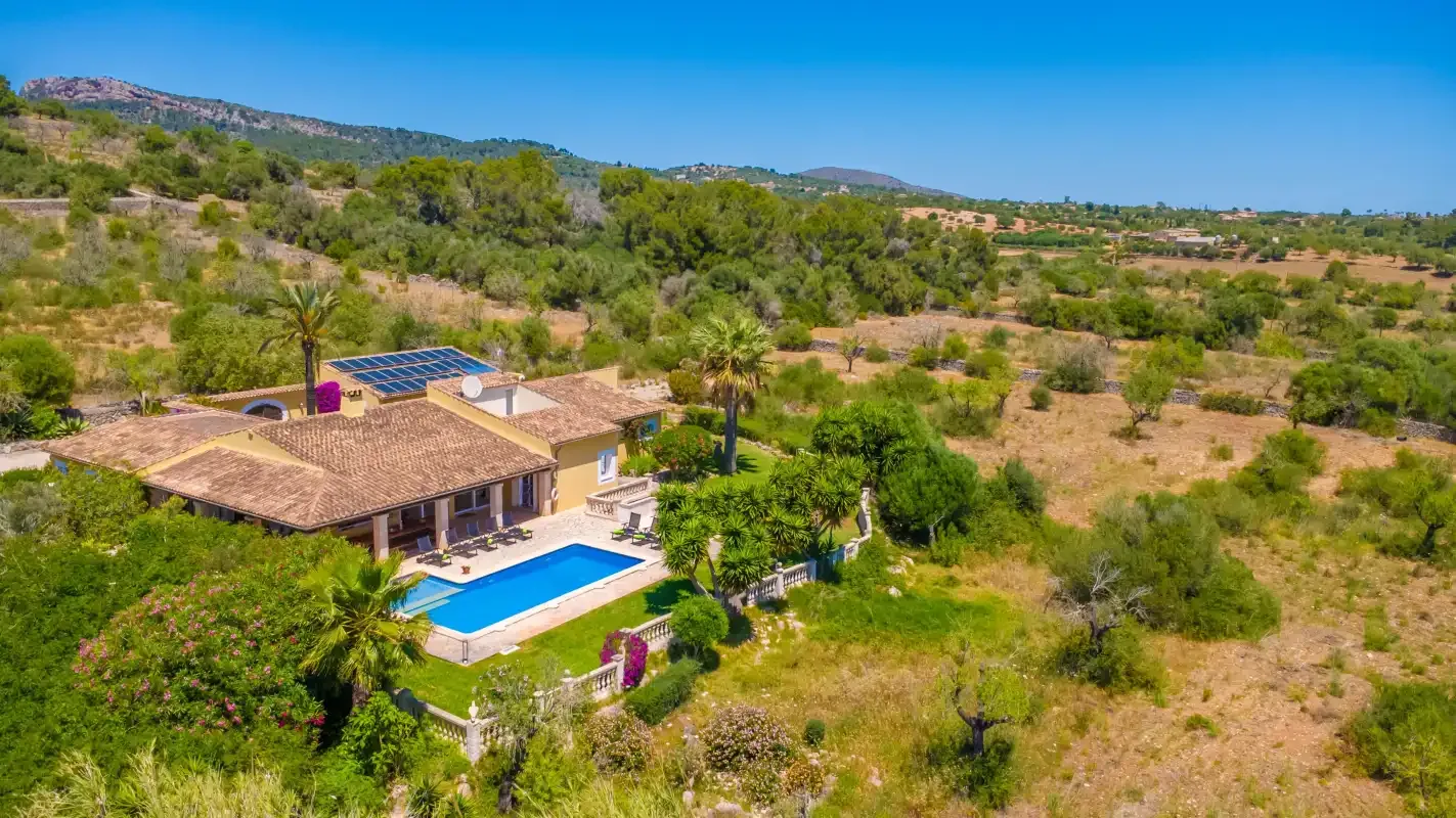Una casa rural con piscina se encuentra entre colinas secas y arboladas.