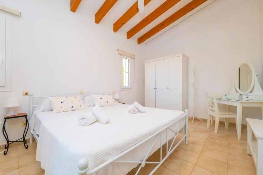 Un dormitorio luminoso con una cama blanca, un armario y vigas de madera a la vista.