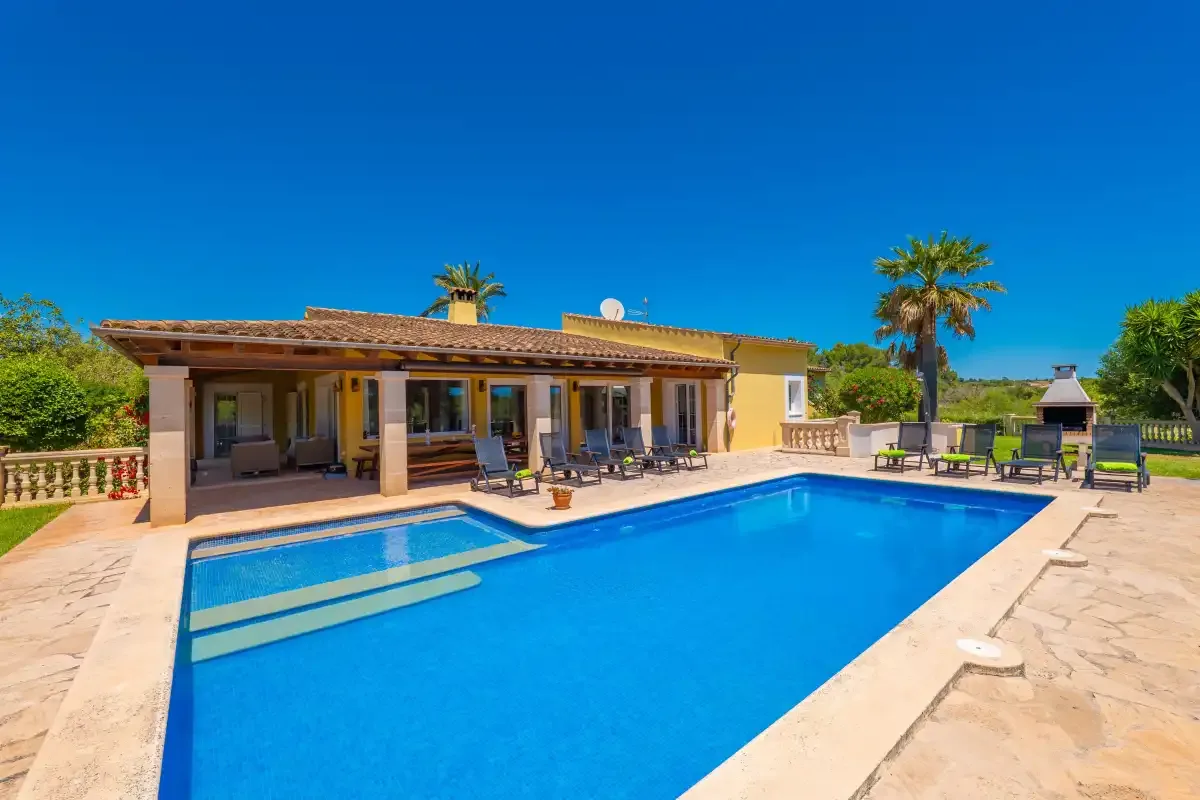 Un patio de villa da a una piscina bajo un cielo azul despejado.