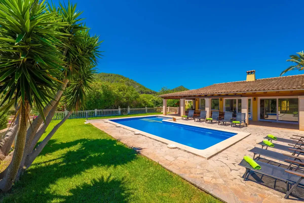 Una piscina junto a una casa de una planta, con patio pavimentado y jardín.