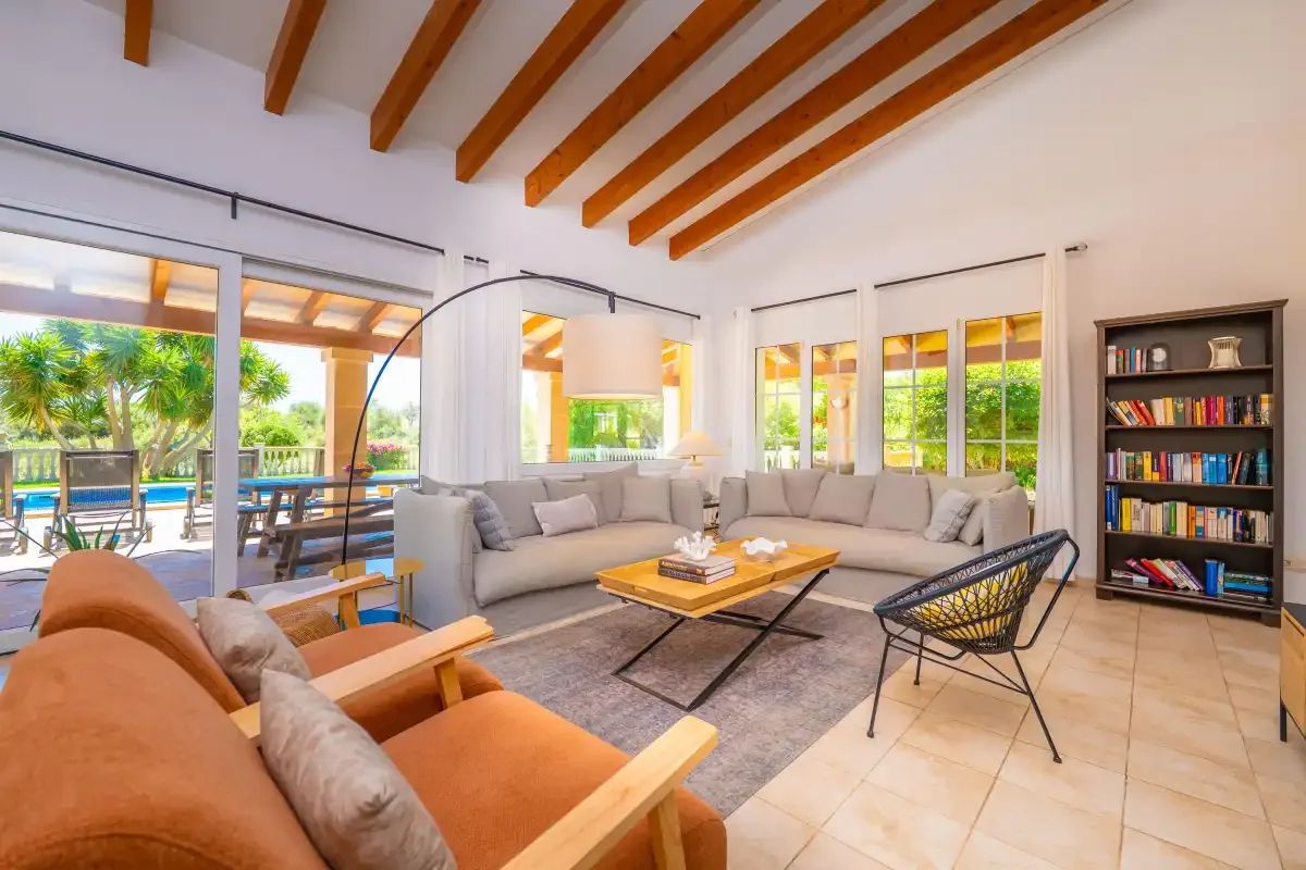 Una sala de estar luminosa con asientos alrededor de una mesa de centro y ventanas grandes.
