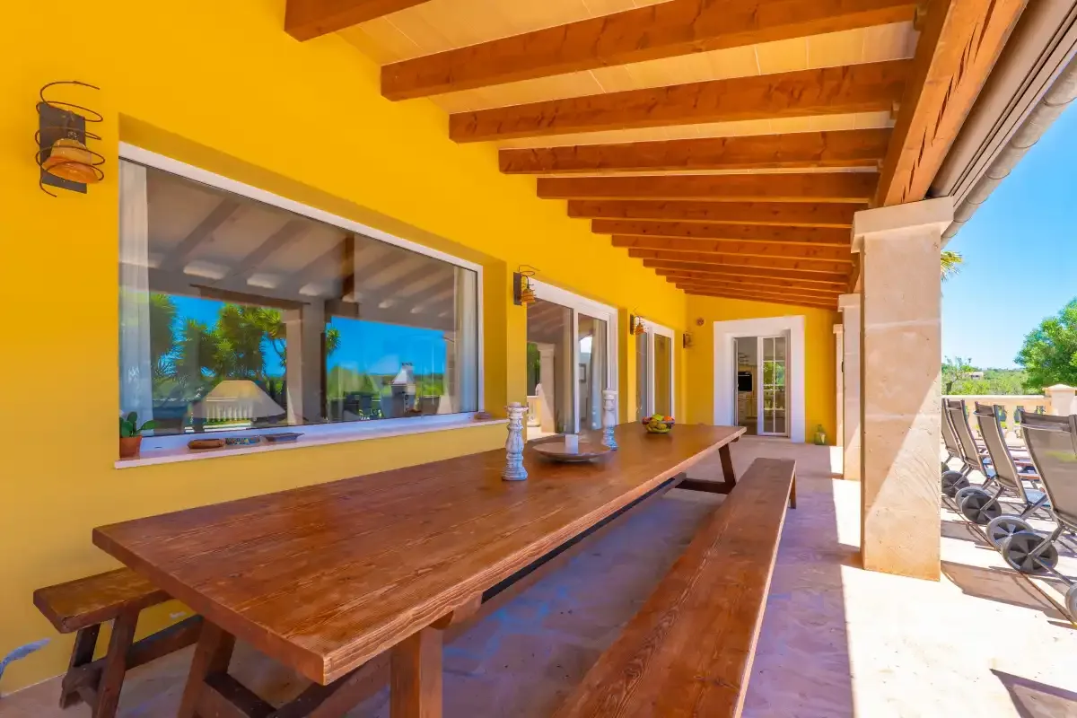 Comedor exterior cubierto con una larga mesa de madera junto a la casa.