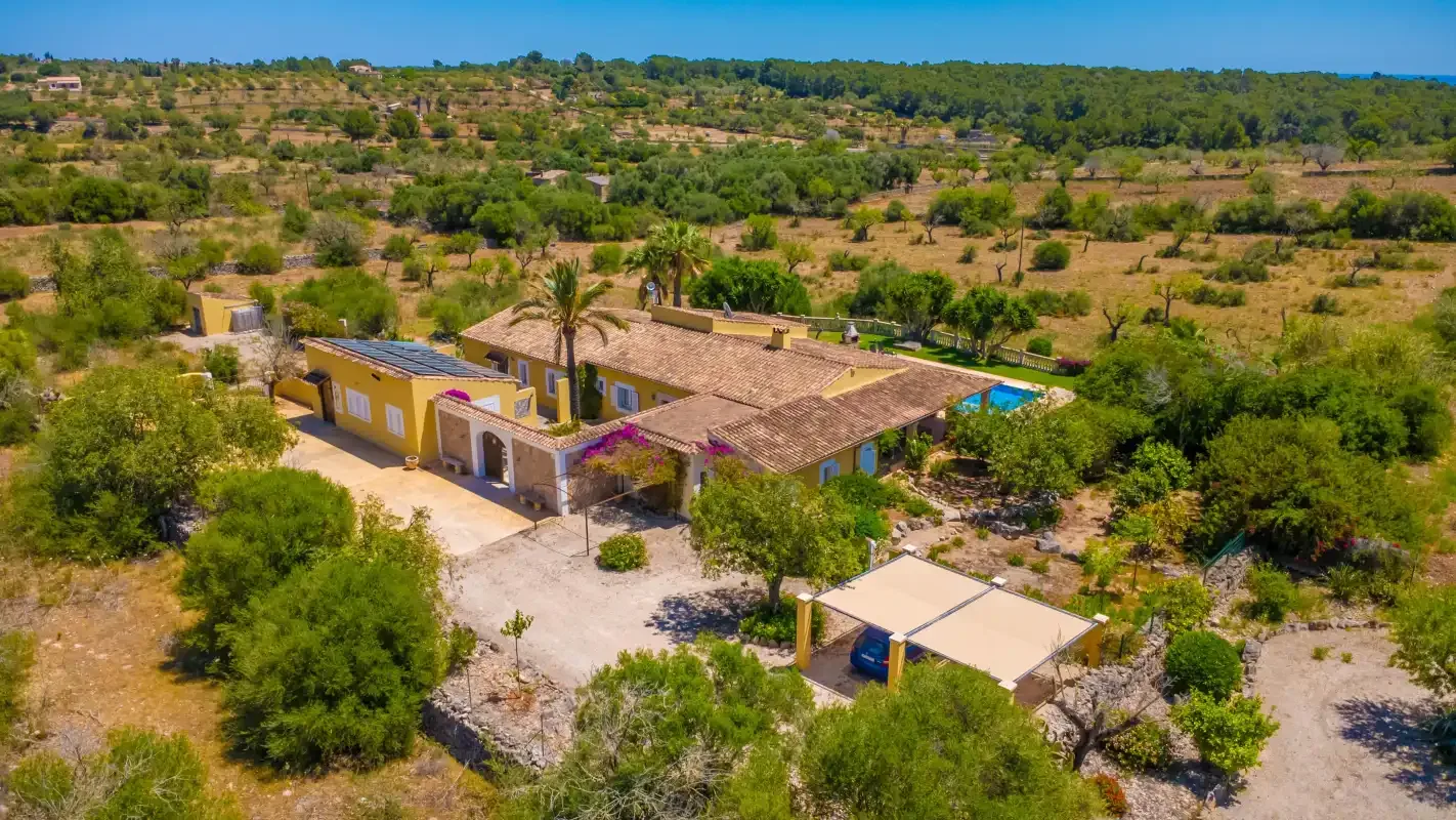 Vista aérea de una casa rural rodeada de árboles y terreno abierto.