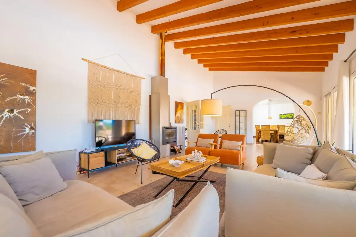 Una sala de estar luminosa con asientos, un televisor y vigas de madera vistas en el techo.