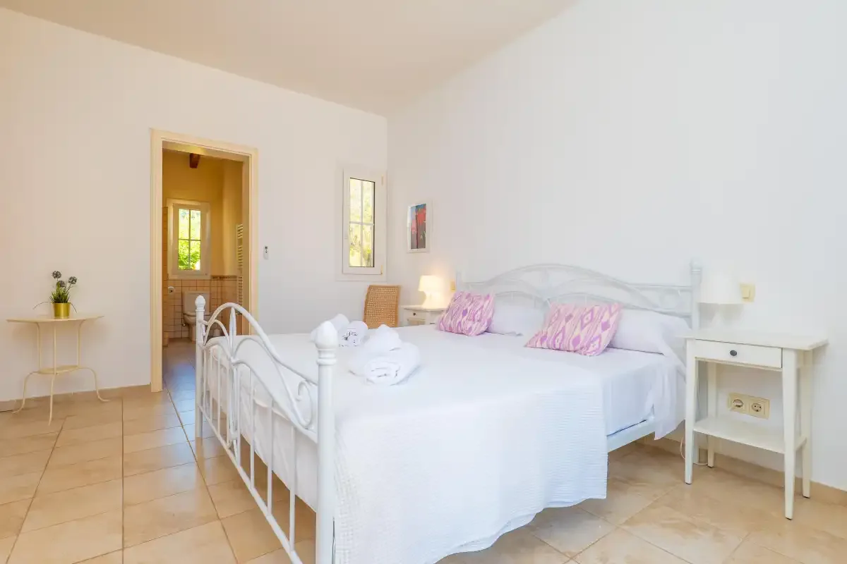 Un dormitorio luminoso con una cama blanca y mesitas de noche.