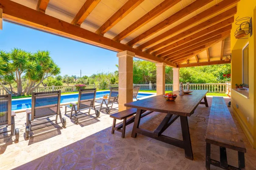 Un patio cubierto con una mesa de comedor de madera da a una piscina.