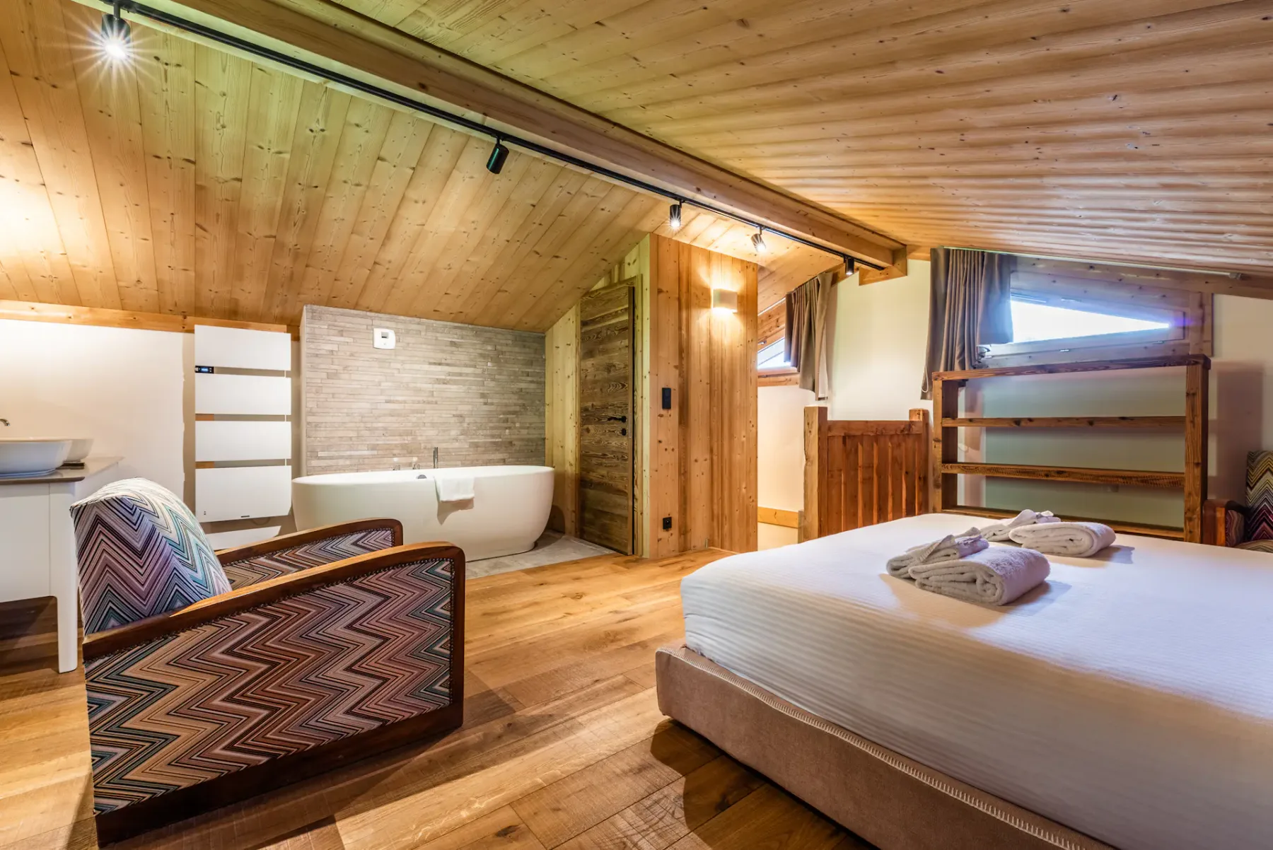 A wood-paneled bedroom with a bed, seating, and a bathtub in the adjoining area.