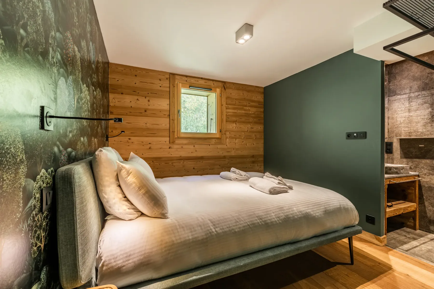A bedroom with a neatly made bed and a small window in the wood-paneled wall.