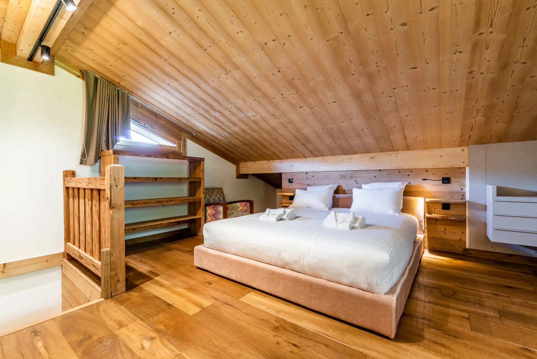 A bedroom with a double bed beneath a sloped wooden ceiling.
