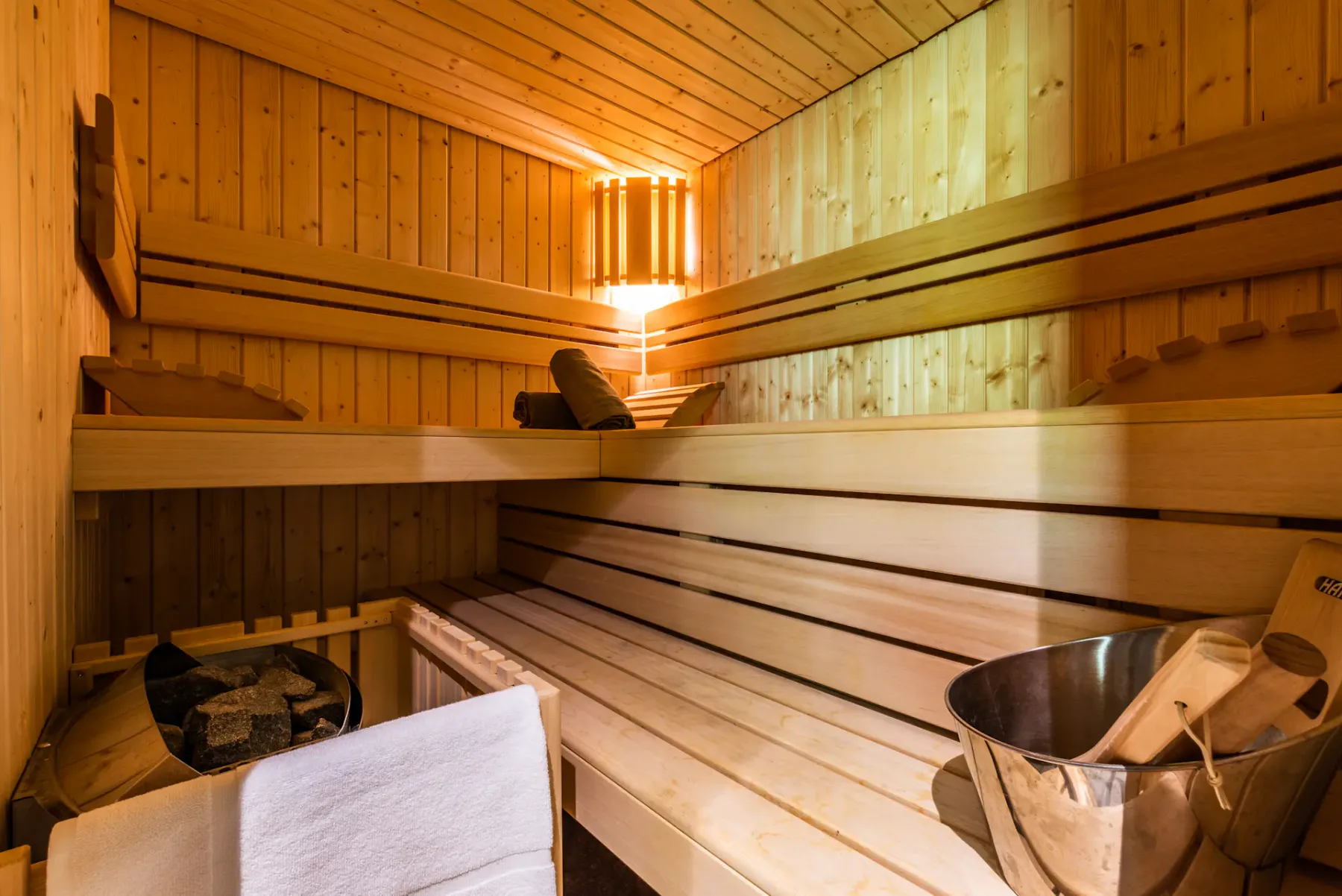 A wooden sauna with tiered seating and a bucket of stones.