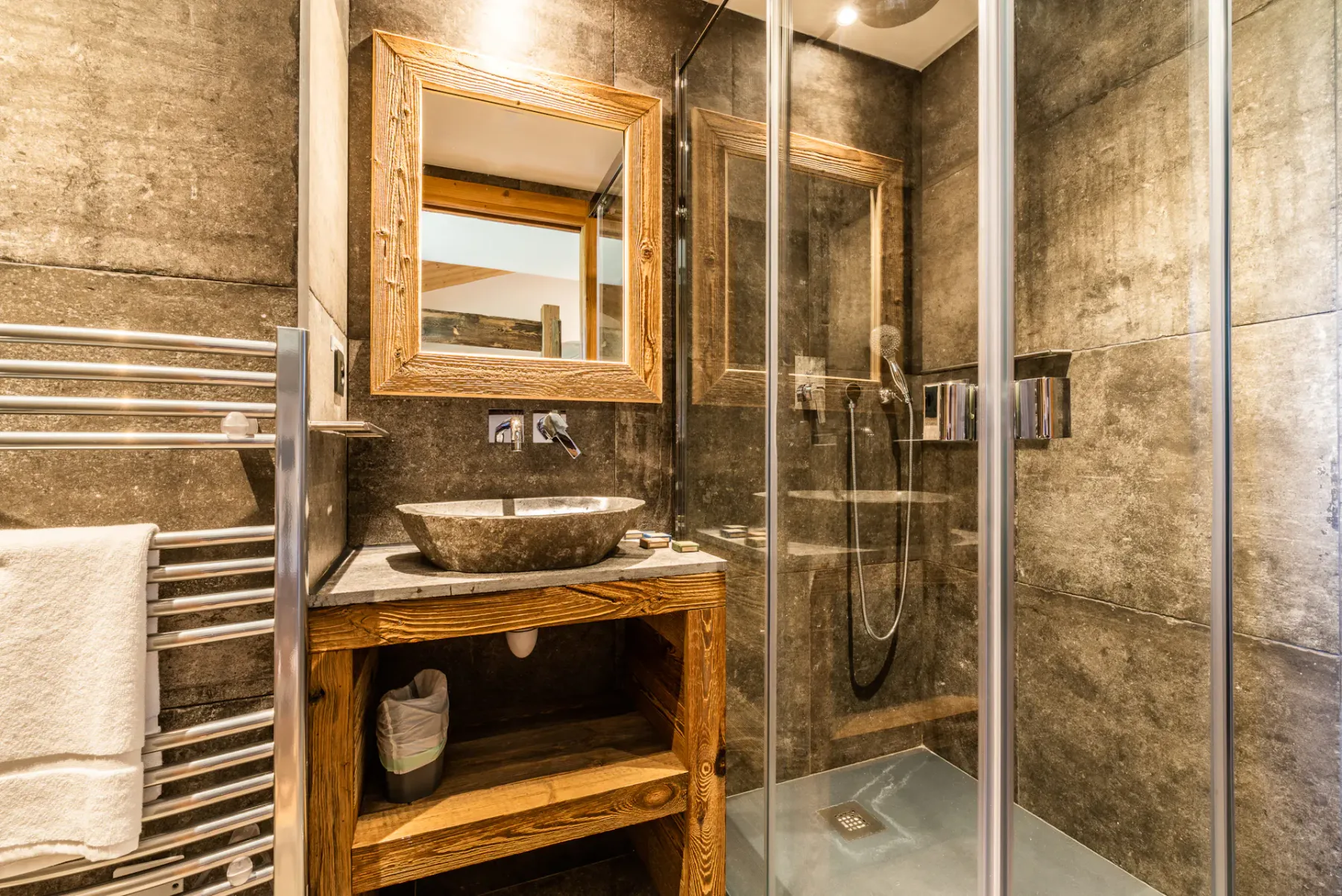 A bathroom with a glass shower and a wooden vanity beneath a mirror.